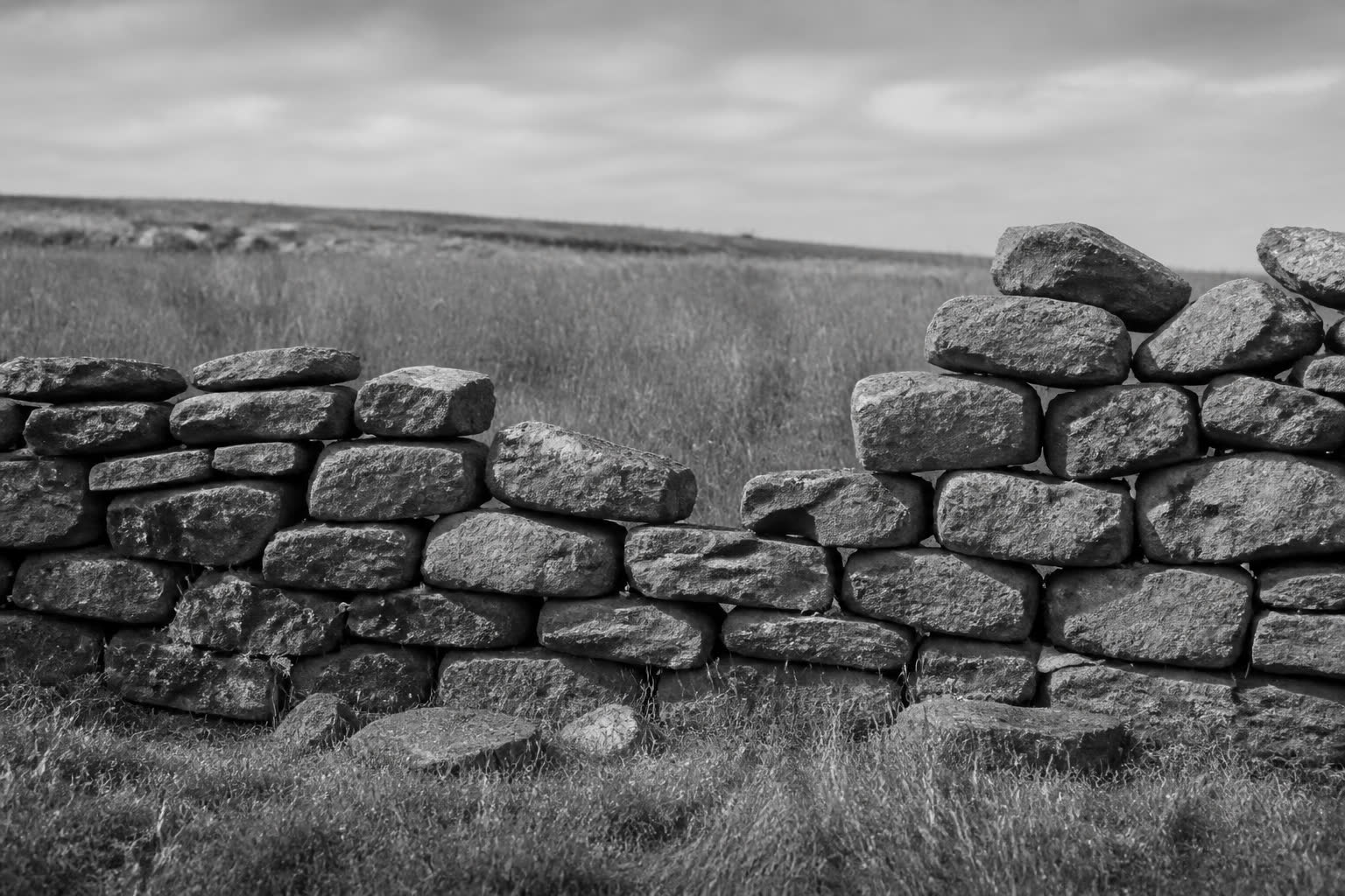 Black-and-white unfinished dry-stone wall with a gap in a field