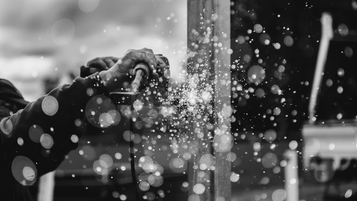 Black-and-white sparks from a grinder against a metal beam in a plant setting