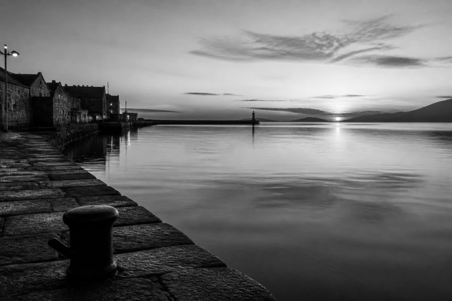 Black-and-white still harbor at dawn with a low sun on the water