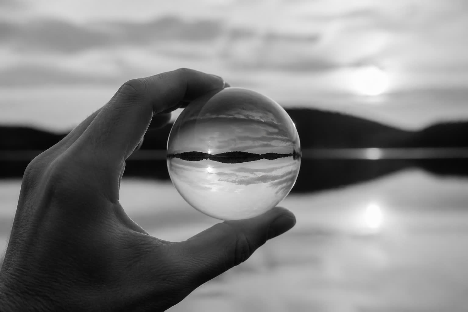 Black-and-white hand holding a glass sphere with an inverted landscape inside