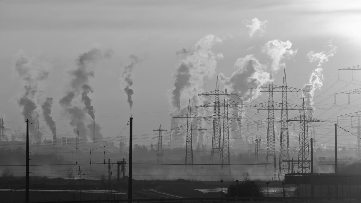 Black-and-white industrial skyline with transmission towers and plant smoke at dusk