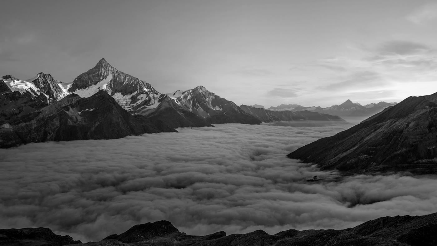 Black-and-white mountain peaks above a sea of clouds at sunrise