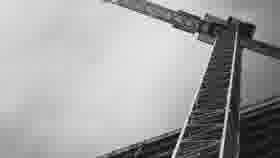 Black-and-white low-angle view of a tower crane and building framework against an overcast sky