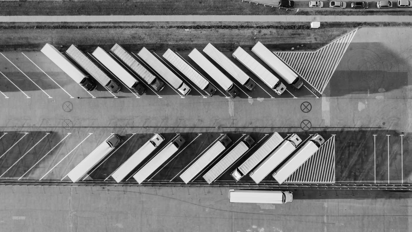 Black-and-white aerial view of semi-trucks parked in angled bays at a logistics lot