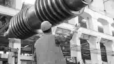 Black-and-white plant floor worker guiding a large suspended industrial machine component