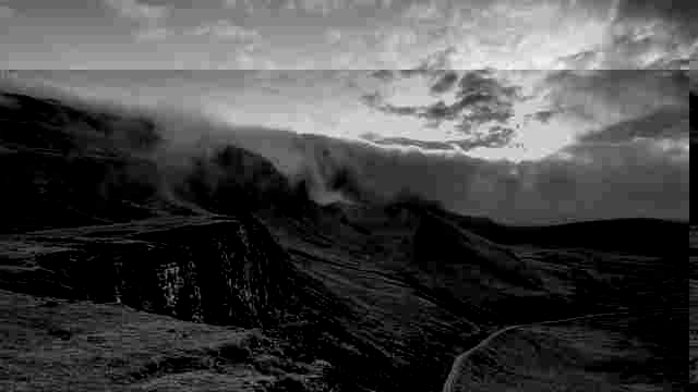 Black-and-white rugged cliffs and valley with fog rolling over mountain ridges