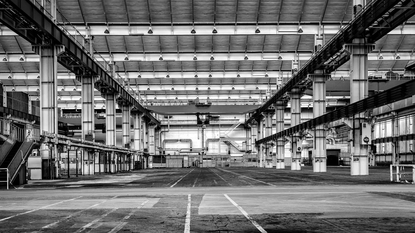 Black-and-white empty factory floor with steel columns, concrete aisle, and overhead crane
